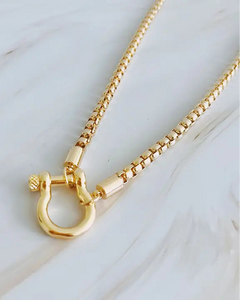 Gold necklace with a unique clasp on a light wooden surface