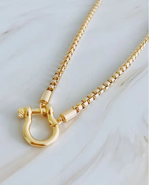 Gold necklace with a unique clasp on a light wooden surface