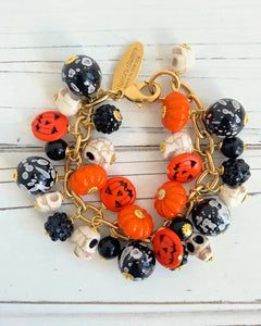 Halloween-themed bracelet with pumpkins, skulls, and gold chain on a white wooden background
