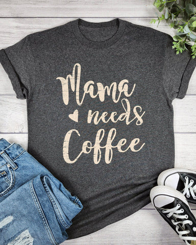 Gray t-shirt with 'Mama needs Coffee' text on a wooden surface with jeans and sneakers.