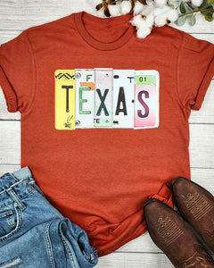 Red t-shirt with 'TEXAS' design on a wooden surface with jeans and boots.